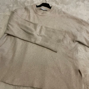 Beige stickad tröja från Bershka - Säljer en stilren beige stickad tröja från Bershka. Tröjan har långa ärmar och ribbade detaljer vid ärmslut och nederkant. Perfekt för kyliga dagar!