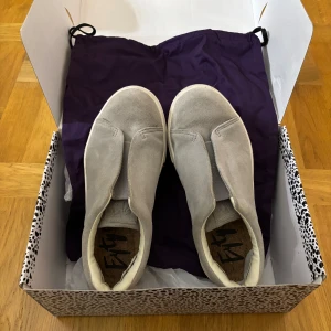 Grå sneakers från Eytys - Snygga grå sneakers från Eytys i mocka med en stilren design. Skorna har en vit sula och en lila detalj baktill. Endast använda fåtal gånger och skicket är bra. Nypris på dessa är 2000 kr. Dustbag och låda medföljer!