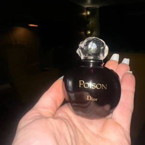 Poison parfym från Dior - Elegant parfymflaska från Dior med namnet Poison. Flaskan är mörklila och har en unik, rundad form med en dekorativ, genomskinlig kork. Perfekt för den som söker en klassisk och mystisk doft.