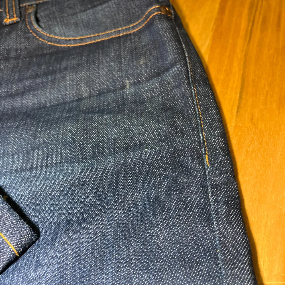 Säljer ett par mörkblå jeans från Nudie Jeans med klassisk femficksdesign och orange sömmar. Perfekta för en stilren look. Model: grim tim, storlek 31/32, finns små fläckar som ej syns på en distans. Farkut & Housut.