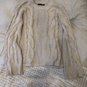 Beige stickad tröja från 157 - Säljer en mysig beige stickad tröja från 157 med flätstickade detaljer längs ärmarna. Tröjan har en rund halsringning och ribbade muddar vid ärmslut och nederkant. Perfekt för kyliga dagar!