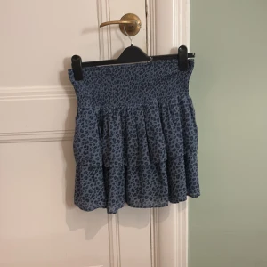 Blå leopardmönstrad kjol från Kappahl  - Snygg blå kortkjol med leopardmönster och volanger från Kappahl. Perfekt för en trendig look. Elastisk midja för bekväm passform.