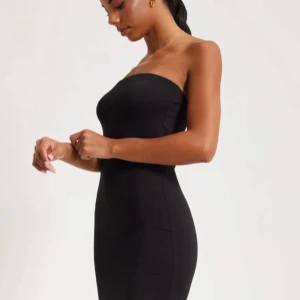 Svart axelbandslös klänning - Elegant svart axelbandslös klänning med en tight passform. Perfekt för en stilren och sofistikerad look. Klänningen har en lång design som ger en smickrande siluett. Använd fåtal gånger, inga defekter!💓💓