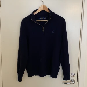 Mörkblå tröja från Polo Ralph Lauren - Säljer en stilren mörkblå tröja från Polo Ralph Lauren med dragkedja vid halsen och det ikoniska logotypbroderiet på bröstet. Perfekt för en klassisk och avslappnad look.