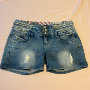 Blå jeansshorts från early 2000 talet - Snygga blå jeansshorts med unika hjärtformade knappar och slitna detaljer. Shortsen har flera fickor och ett coolt randigt innerfoder i midjan. Dom är vintage. Skriv gärna för måtten då jag inte är säker på deras storlek.