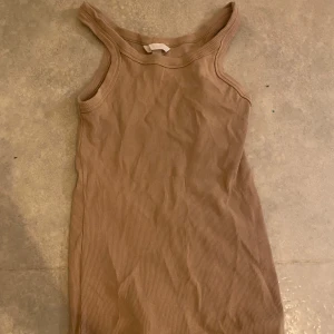 Beige ribbat linne från H&M - Säljer en stilren beige ribbat linne från H&M. Den är ärmlös och har en tight passform som framhäver figuren. Perfekt för en avslappnad och trendig look.