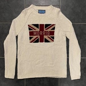 Vit stickad tröja från Morris - Snygg vit stickad tröja från Morris med Union Jack-motiv och texten 'Morris' på bröstet. Tröjan är tillverkad i 100% bomull och har långa ärmar. Perfekt för en stilren och avslappnad look.
