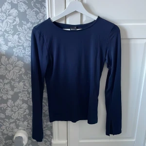 Marinblå långärmad tröja - Säljer en marinblå långärmad tröja med en öppning vid handleden. Enkel att matcha med olika outfits. Tröjan har en klassisk design med rund hals och är tillverkad i ett mjukt material.