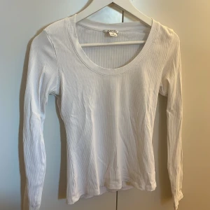 Vit ribbad tröja från Monki - Säljer en stilren vit ribbad tröja från Monki i storlek M. Tröjan har en rund halsringning och långa ärmar, perfekt för lager-på-lager eller som den är. Ett mångsidigt plagg för garderoben!