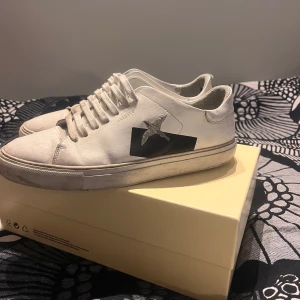 Vita sneakers från Axel Arigato - Snygga vita sneakers från Axel Arigato med svart detalj och fågel på sidan. Skorna har snörning och en klassisk design som passar perfekt till vardagsstilen. Använda inte längre och vill bli av med dem för billigt pris