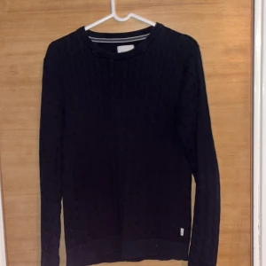 Svart tröja från Jack & Jones - Säljer en stilren mörkblå tröja från Jack & Jones. Tröjan har ett kabelstickad mönster och är perfekt för en snygg och avslappnad look. Den är långärmad och har en rund halsringning. Nypris: 500kr. Mitt pris: 250kr.                                      Vid frågor är det bara att höra av sig😃