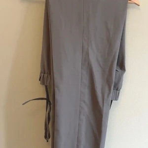 Grå byxor från COS - Snygga grå byxor från COS med en stilren design. Byxorna har en rak passform och är tillverkade i en blandning av ull och polyester, vilket ger en bekväm och elegant känsla. Perfekta för en stilren look.