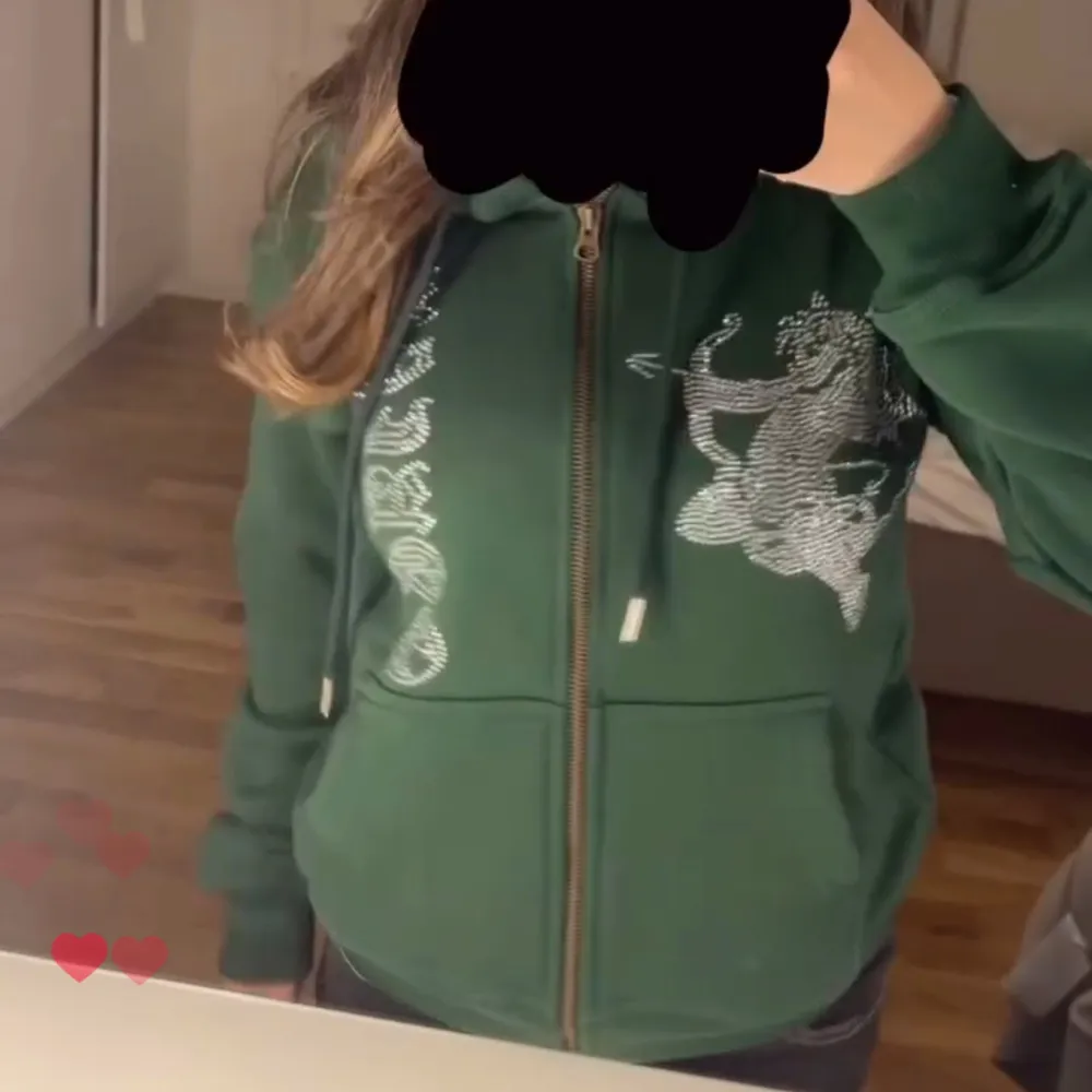 Säljer en grön hoodie med dragkedja med en textdesign på framsidan med rhinestones. Den har en luva och två fickor fram. Perfekt för en avslappnad och bekväm stil. Passar bra till jeans eller andra casual outfits. storlek : S. nypris ligger på 700kr men säljer för 400-500kr💚märke - laviago. Tröjor & Koftor.