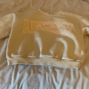 Beige tjocktröja  - Beige tjocktröja får de står kindness med orange text över tröjan från Lindex i storlek 146/152