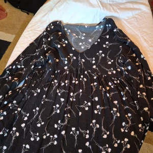 Svart blommig klänning - Säljer en superfin svart klänning med vita blommor. Den har en v-ringad hals och är långärmad. Klänningen är perfekt för både vardag och fest. Materialet känns mjukt och bekvämt. Passar bra till höst och vår.