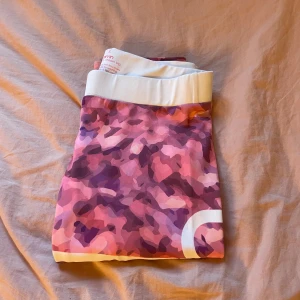 Camouflage mönstrade leggings från Aim'n - Säljer ett par snygga och bekväma leggings från Aim'n i storlek S De har ett coolt rosa och lila camouflage mönster och en bred vit midja med Aim'n-loggan. Perfekta för träning eller en avslappnad dag. De är i bra skick och redo för en ny ägare!