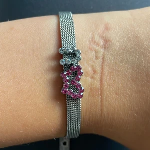 Snyggt armband med nalleberlock - Säljer ett armband i silverfärgat metallnät med två avtagsbara berlocker på. Armbandet har ett justerbart spänne för perfekt passform. Perfekt accessoar för både vardag och fest!