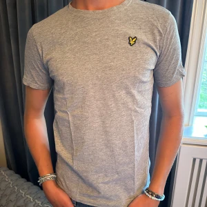 Grå t-shirt från Lyle & Scott - Säljer en snygg grå t-shirt från Lyle & Scott. Den är i nyskick och har en normal passform. T-shirten är gjord av bomull och har en liten broderad logga på bröstet. Perfekt för vardagsbruk!