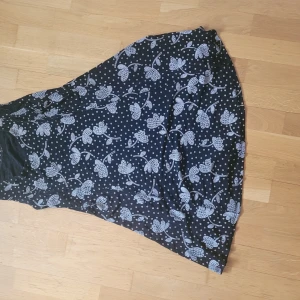 Svart blommig klänning - Säljer en superfin svart klänning med vita blommor och prickar. Klänningen är ärmlös och har en normal passform. Perfekt för sommarens alla fester eller en dag på stan. Materialet känns som bomull och den är väldigt bekväm att ha på sig. Köp den nu och var redo för sommaren! 🌸