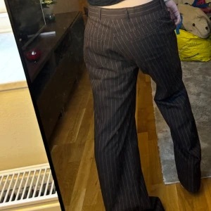 Bruna randiga kostymbyxor - Säljer ett par snygga bruna kostymbyxor med vita ränder. De har en klassisk passform med raka ben och låg midja. Säljer då de tyvärr är för stora för mig! 💕 