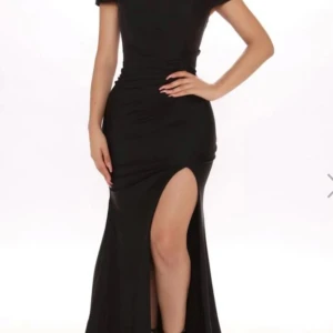 Svart långklänning med slits - Säljer en elegant svart långklänning med en snygg slits framtill. Klänningen har en offshoulder-design som ger en stilren look. Perfekt för fest eller bal! Materialet ser ut att vara mjukt och följsamt, vilket ger en smickrande passform.❤️