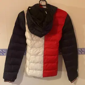 Säljer en snygg pufferjacka från Tommy Hilfiger i rött, vitt och blått. Jackan har en quiltad design och är perfekt för kyligare dagar. Perfekt för både höst och vinter! Helt ny! Storlek xxs dam. Nypris 2999:-