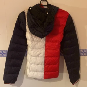 Flerfärgad pufferjacka - Säljer en snygg pufferjacka från Tommy Hilfiger i rött, vitt och blått. Jackan har en quiltad design och är perfekt för kyligare dagar. Perfekt för både höst och vinter! Helt ny! Storlek xxs dam. Nypris 2999:-