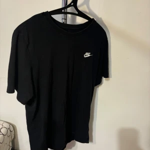 Svart t-shirt från Nike - Säljer en klassisk svart t-shirt från Nike. Den har en enkel design med Nike-loggan i vitt på bröstet. Perfekt för vardagsbruk eller träning. T-shirten är kortärmad och gjord i ett bekvämt material. Har använt ett par gånger! Nypris: 299
