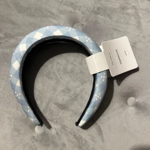 Blått diadem med rutigt mönster - Säljer ett supergulligt diadem från Accessorize i en härlig ljusblå färg med vitt rutigt mönster. Diademet är vadderat för extra komfort och har en stilren design. Märket är By Malina och nypris är 400kr och det är helt oanvänt!