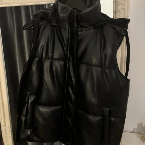 Väst med stor luva - Fin svart läder väst med stor luva. Har ett hål i fickan men påverkar inget. Står storlek 44 men är absolut inte större än m. Kom med prisförslag .