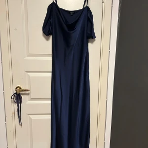 Långklänning  - Marinblå långklänning med friaaxlar. Har en liten slitt på sidan och en dragkedja på sidan under ena armen. 
