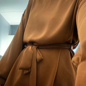 Brun blus från Bik Bok - Säljer en snygg brun-koppar blus från Bik Bok i storlek L. Den har långa ärmar och ett knytband i midjan för en fin passform. 