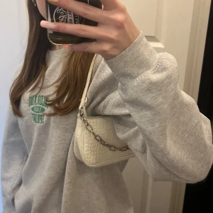 Vit axelväska med kedjedetalj - Säljer en superfin vit axelväska med krokodilpräglat mönster. Väskan har en cool kedjedetalj i silver och en dragkedja upptill. Perfekt för att ge din outfit en extra touch! 👜✨