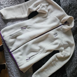 Vit fleecejacka från Haglöfs - Säljer en supermysig vit fleecejacka från Haglöfs i storlek S. Den har en snygg lila dragkedja och matchande detaljer. Perfekt för kyliga höst- och vinterdagar. Jackan är i nyskick och redo för nya äventyr!