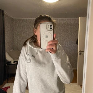 Grå hoodie från Gina Tricot  - Säljer en grå hoodie från Gina Tricot med texten 'Ma Chérie' och en krona tryckt på framsidan. Tröjan har en klassisk design med huva och långa ärmar. Perfekt för en avslappnad stil. Stort tryck på baksidan, se bild 3