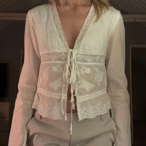 Vit blus från Zara - Säljer en tunn elegant vit blus från Zara med spetsdetaljer och knytning framtill. Blusen har en v-ringad design och ärmar med slits, perfekt för en stilren look nu till våren och sommaren🤍