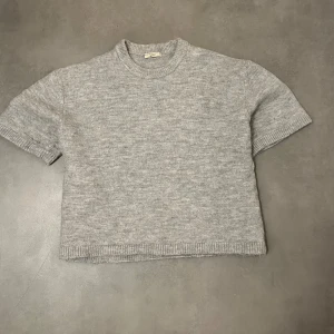 Grå stickad tröja från Gina Tricot - Säljer en stilren grå stickad tröja från Gina Tricot i premiumkvalitet. Tröjan har korta ärmar och en rund halsringning med ribbade kanter. Har knappt använt. Hör av för frågor🩷