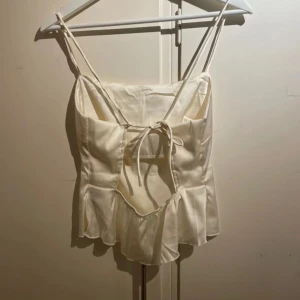 Öppen rygg - Säljer ett elegant satinlinne med smala axelband och volangdetalj nedtill. Toppen har en öppen rygg med knytning för en stilren look. Perfekt för sommarens alla stunder, liten i storlek 