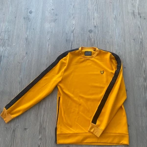 Gul tröja från Lyle & Scott - Säljer en snygg gul tröja från Lyle & Scott med svarta detaljer längs ärmarna. Tröjan är helt o använd vilket kan ses på bilderna, skriv om ni funderar på något!