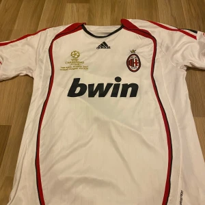 Vit AC Milan 2006 retro kaka fotbollströja från Adidas - Säljer en vit AC Milan fotbollströja från Adidas med röda och svarta detaljer. Tröjan har korta ärmar och klubbens emblem på bröstet. Den har även Champions League-märke och sponsorlogga på framsidan. Nummer och namn 'KAKA 22' på baksidan. Den är size l men passar M och S eftersom den är playerfit 
