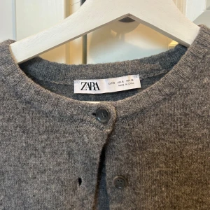 Grå kofta från Zara - Säljer en stilren grå kofta från Zara i storlek S. Koftan har långa ärmar och knappar framtill. Den är tillverkad i ett mjukt material som ger en bekväm passform. Knappt använd. 