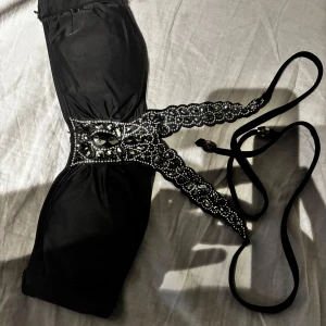 Svart bikini överdel - Elegant svart bikini med vackra spetsdetaljer och glittrande pärlor. Den har en unik design med snörning och dekorativa band. 