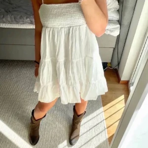 Vit sommarklänning - Säljer en söt vit sommarklänning med smockad överdel och tunna axelband. Klänningen har en volangdetalj vid fållen som ger en lekfull känsla. Perfekt för varma dagar och avslappnade tillfällen. 🌞