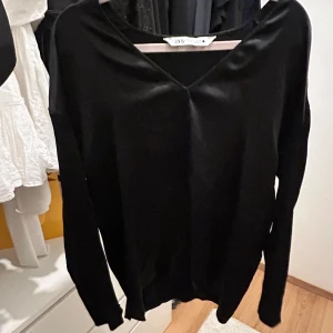 Svart tröja från Zara - Snygg svart tröja från Zara med v-ringad design. Perfekt för en stilren look. Tröjan har långa ärmar och är gjord i ett mjukt material.