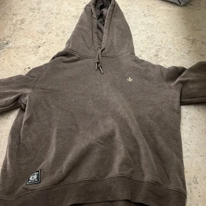 Brun hoodie från Morris - Säljer en brun hoodie från Morris med en liten broderad detalj på bröstet. Tröjan har en justerbar huva med snören och en mjuk insida. Perfekt för kyliga dagar!