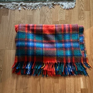 Rutig filt med fransar - Säljer en färgglad rutig filt med fransar i ändarna. Filten har en mix av rött, blått, grönt och orange i ett klassiskt rutmönster.