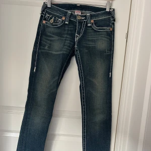 Mörkblå jeans från True Religion - Snygga mörkblå jeans från True Religion med kontrasterande vita sömmar och klassiska bakfickor med knappar. Jeansen har en låg midja och en straight passform 
