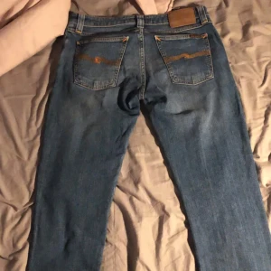 Blå jeans från Nudie Jeans - Säljer ett par snygga, trendiga blå jeans från Nudie Jeans med klassisk femficksdesign och orange sömmar. De har en slim passform och är i storlek W29. 