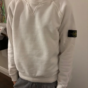 Vit tröja från Stone Island Junior  - Säljer en stilren vit tröja från Stone Island Junior. Tröjan har en klassisk design med långärmade ärmar och en rund halsringning. Tröjan är använd ett fåtal gånger!