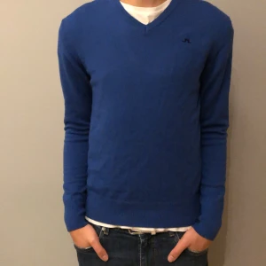 Tröja från J.Lindeberg - Snygg blå tröja från J.Lindeberg med v-ringning. Perfekt för en stilren look. Tröjan har långa ärmar och en diskret logga på bröstet, bakom nacke och vänster arm. Storlek L men skulle säga passar s/m. Vid funderingar är det bara att skriva